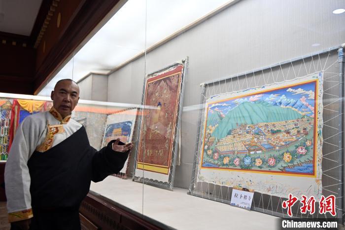 图为交巴加布展示以拉卜楞寺为主题的唐卡作品。交巴加布不仅继承了传统唐卡技艺，更在创新中展现了个人特色。他结合现代审美和绘画技巧，使作品既保留了传统的韵味，又具有鲜明的现代气息。这种独特的艺术风格使他的作品在众多唐卡中脱颖而出，成为藏族民众和艺术爱好者争相收藏的艺术珍品。九美旦增 摄

